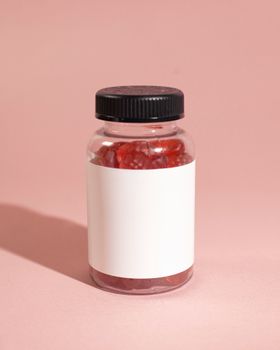 A clear bottle filled with red gummies on a pink background, ideal for product mockups.