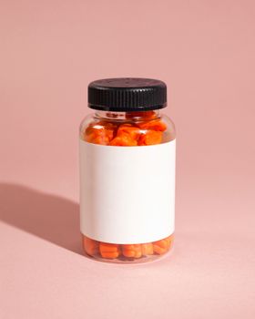 Close-up of a clear bottle filled with orange gummies on a pink background, offering ample copyspace.