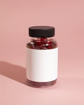 Minimalist product shot of a clear vitamin bottle on pink background.