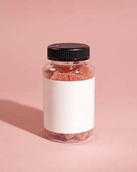 Clear jar of gummy vitamins with a blank label on a pink background, ideal for mockups.