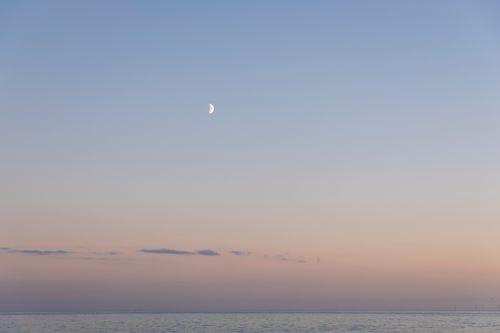 Free A tranquil seascape with a half moon in a pastel twilight sky above a calm sea. Stock Photo