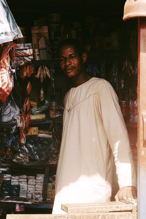 Free A man in traditional attire stands inside a bustling market stall in Abuja, Nigeria. Stock Photo