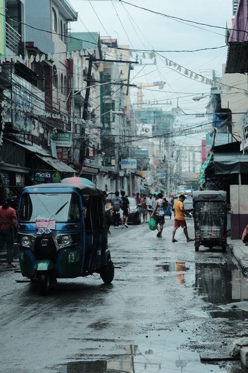 Free A dynamic city street scene featuring tuk-tuks and people under an overcast sky. Stock Photo