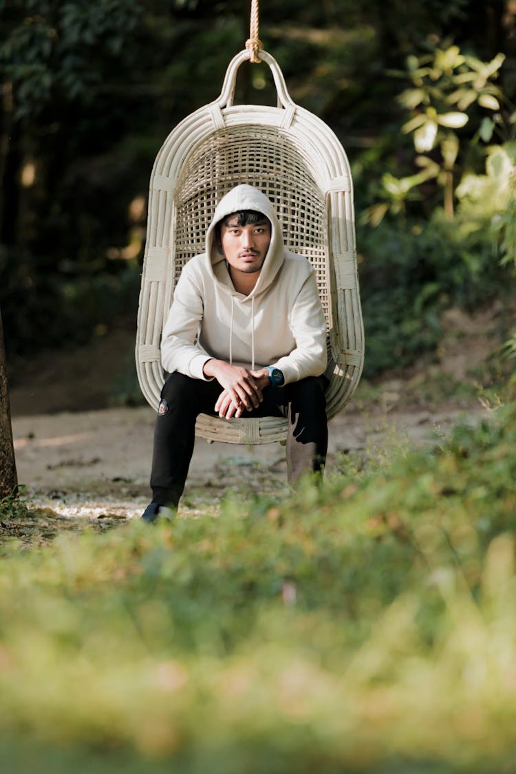 Man Sitting In Hanging Chair In Garden