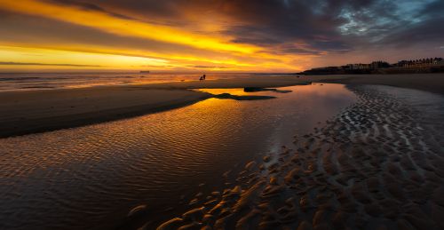 Free A serene beach at sunset with vibrant orange skies and calm waters reflecting the evening glow. Stock Photo