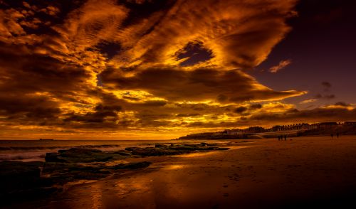 Free A stunning beach sunset with dramatic golden clouds and rocky shore. Stock Photo
