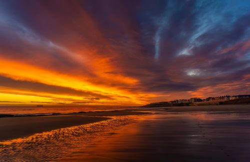 Free Stunning orange sunset over a serene beach with dramatic cloud formations and ocean reflections. Stock Photo