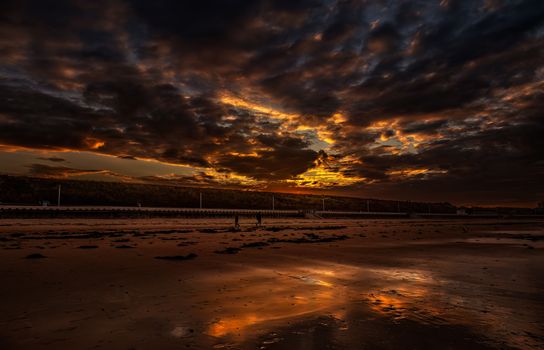 Epic sunset with fiery clouds reflecting on the beach, creating a serene and dramatic landscape.