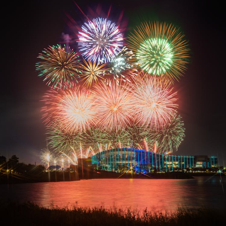 Colorful Fireworks Over A Building Near A Body Of Water