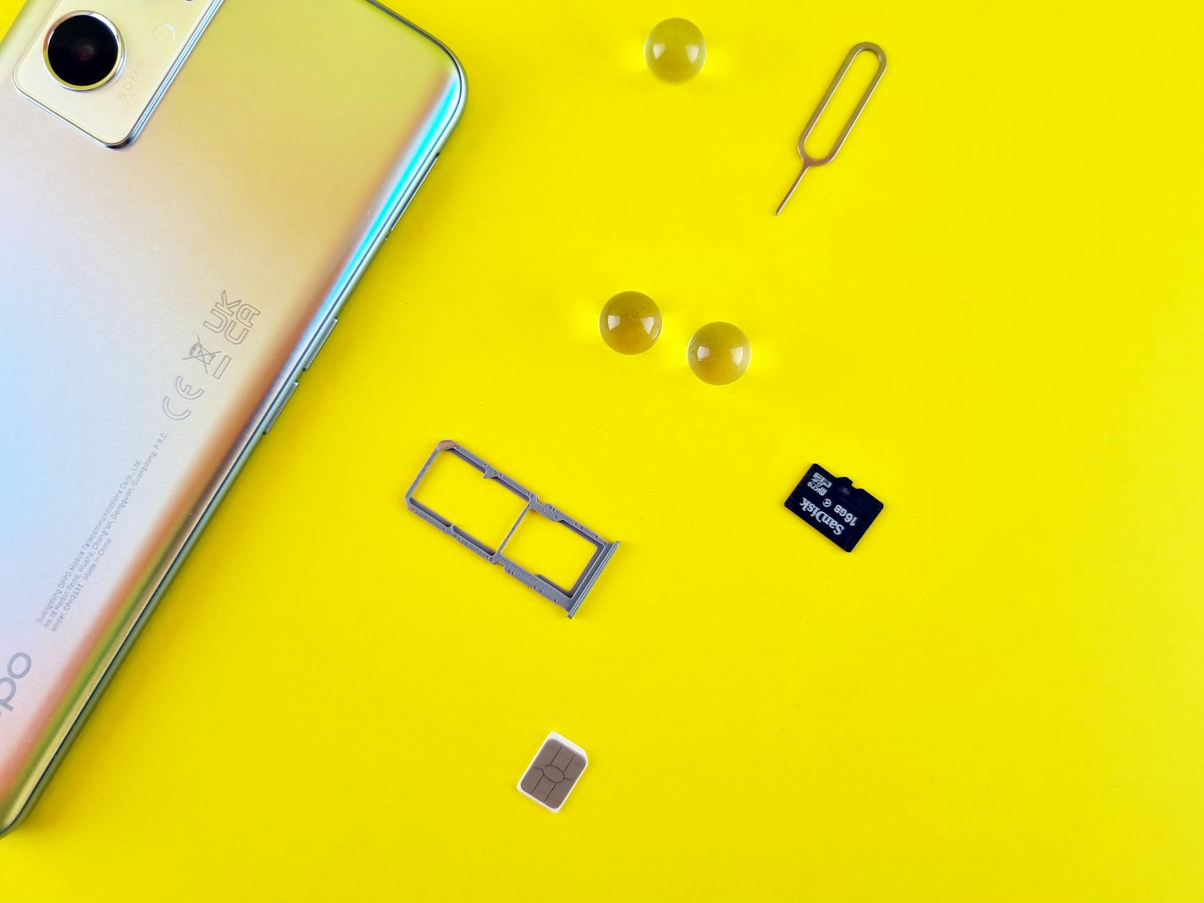 Close-up of a mobile phone with a SIM card, SIM tray, and memory card on a vibrant yellow surface.