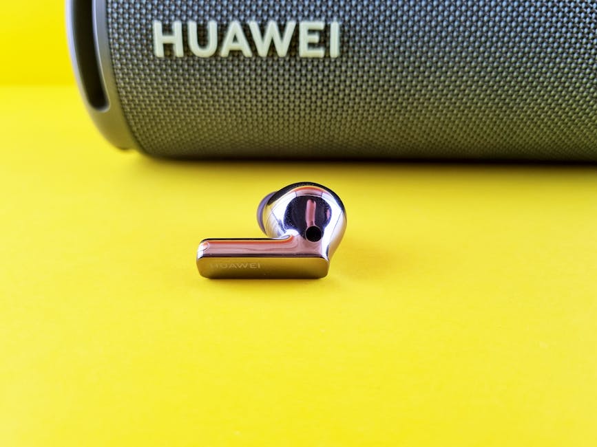 Close-up of a Huawei wireless earbud with a speaker on a vibrant yellow surface for tech and audio representation.