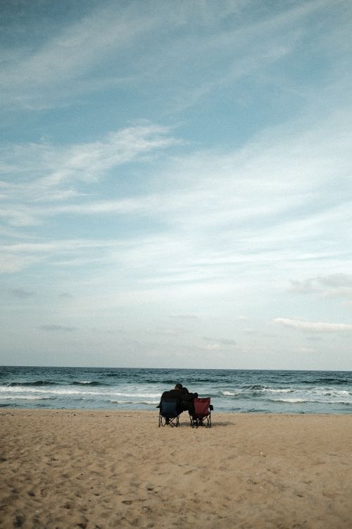Free A serene moment of a couple embracing on a sandy beach with sea waves in the background. Stock Photo