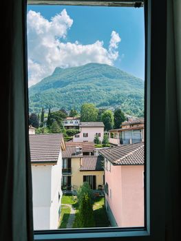 Charming view of Lugano's hills and rooftops framed by a window in summer.