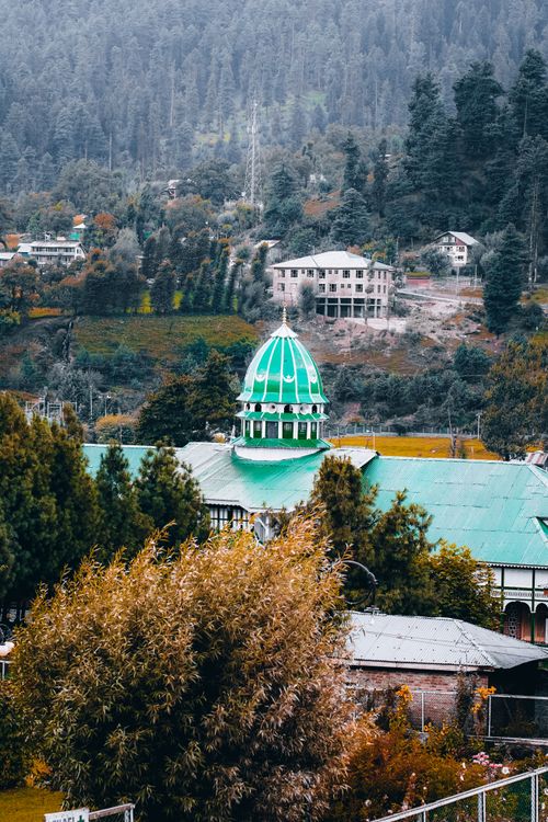 Free Picturesque mountain village with unique green domed roof amidst lush greenery and tall trees. Stock Photo