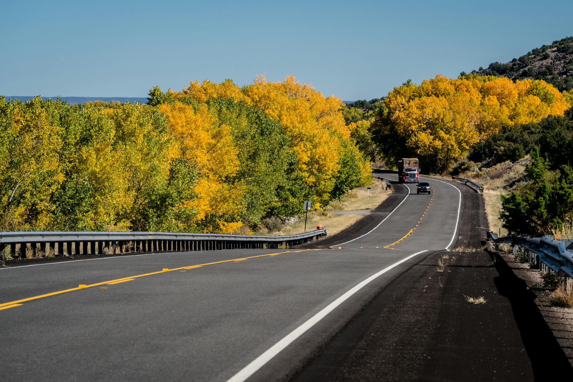 Scenic autumn drive through Ojo Caliente, New Mexico with vibrant fall foliage and empty highway.