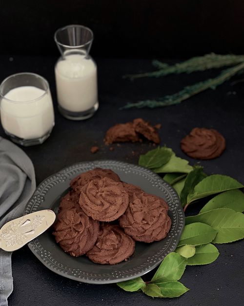 Free Indulge in rich chocolate cookies with milk, presented on a ceramic plate, surrounded by green leaves in a stylish setup. Stock Photo