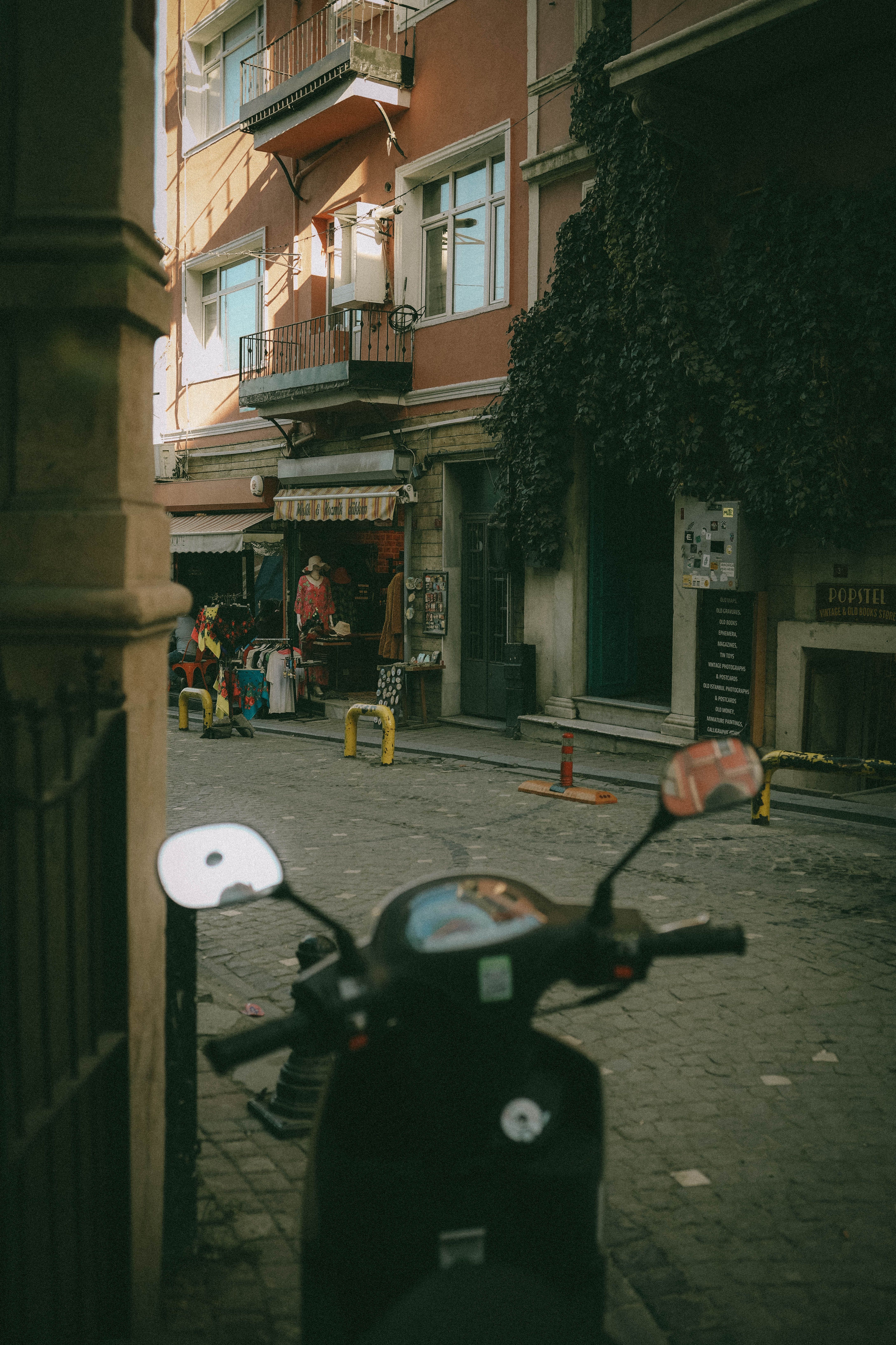 Explore a quaint Istanbul alley featuring a moto scooter and vibrant local shops, framed by Ivy-clad buildings.