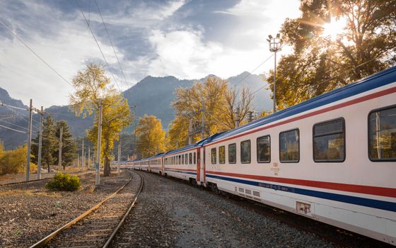 A picturesque train travels through a vibrant autumn landscape with mountains.