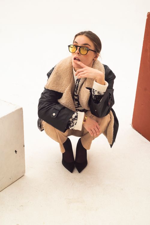 Free Fashionable woman crouching with sunglasses and layered winter outfit against a white background. Stock Photo