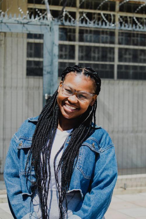 Free Portrait of a smiling young woman with braided hair and glasses in a denim jacket outdoors. Stock Photo