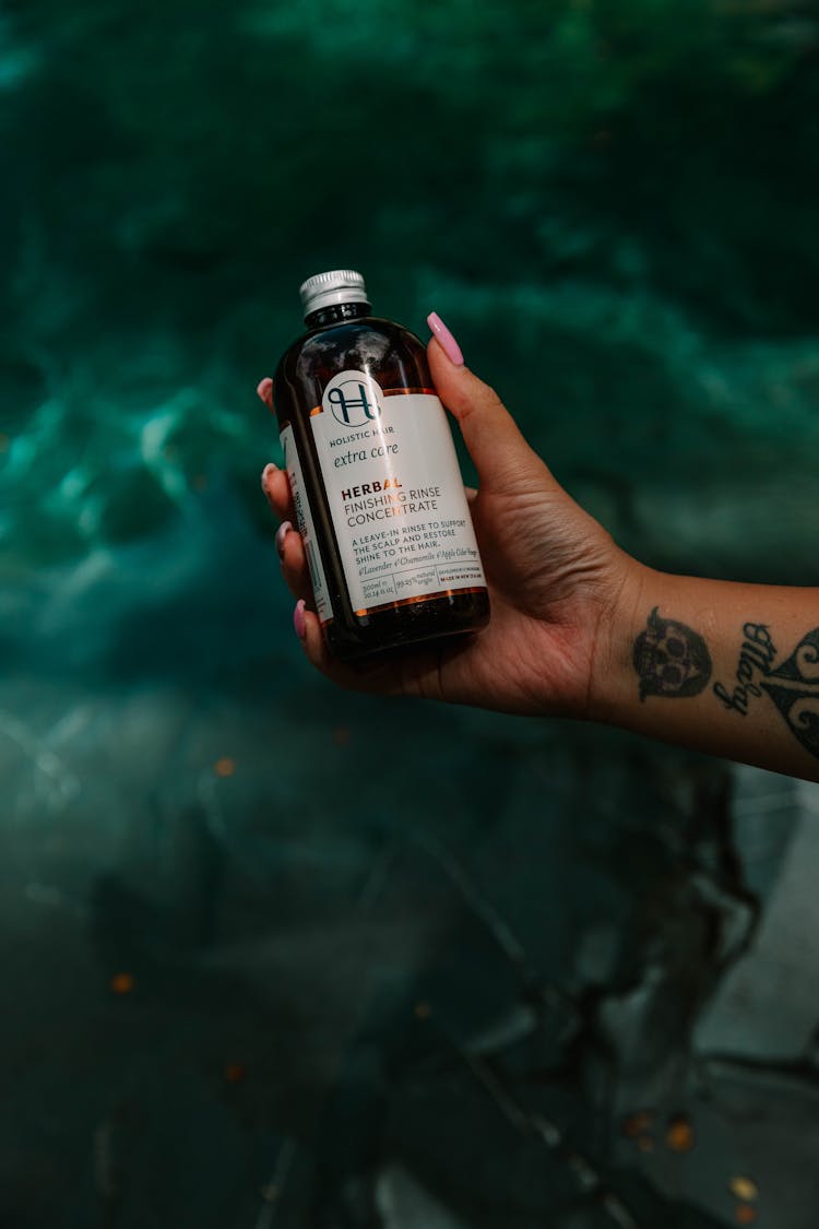 A Hand Holding A Herbal Medicine In A Glass Bottle