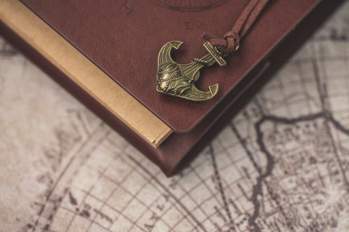 Free A vintage-themed notebook with an anchor ornament resting on an old map, evoking exploration and adventure. Stock Photo
