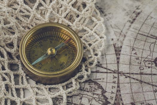 Brass compass resting on an antique world map with crochet details, symbolizing navigation and exploration.