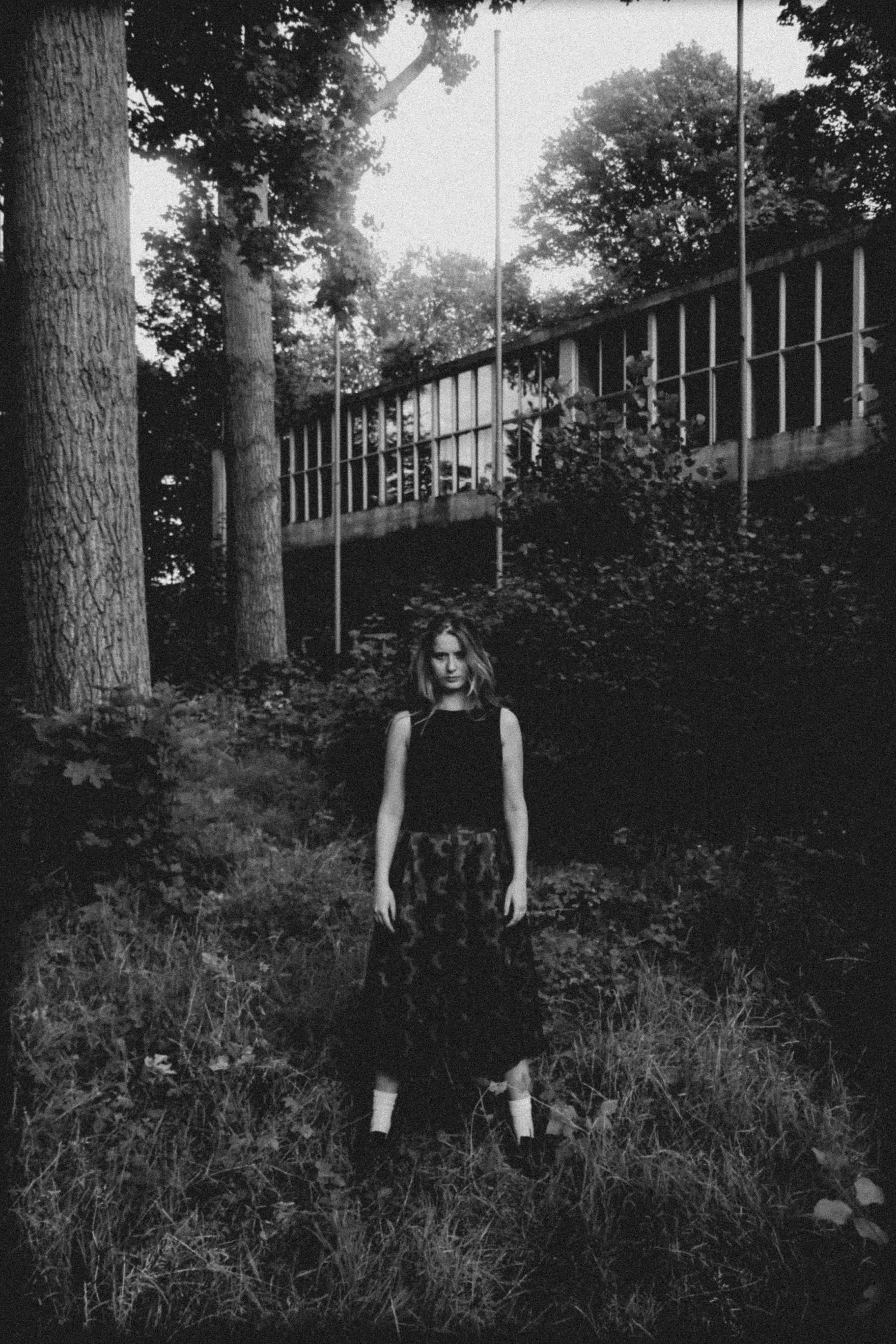 A woman stands in a grayscale forest setting, evoking a moody atmosphere.