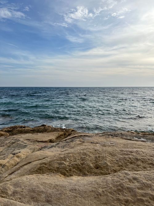 Free A tranquil view of a rocky coastline meeting the vast ocean under a clear sky. Stock Photo