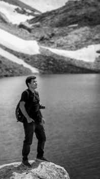 Man stands on rock by a serene mountain lake, minimalist black and white photo.