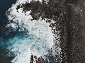Aerial shot of waves crashing on rocky shore at Playa de Las Americas, Spain.