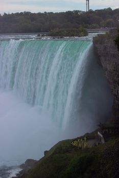 Dramatic capture of Niagara Falls with mist and lush greenery from the Canadian side.