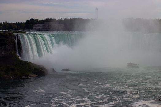 Capture of Niagara Falls with mist and a tourist boat, showcasing natural beauty and adventure.