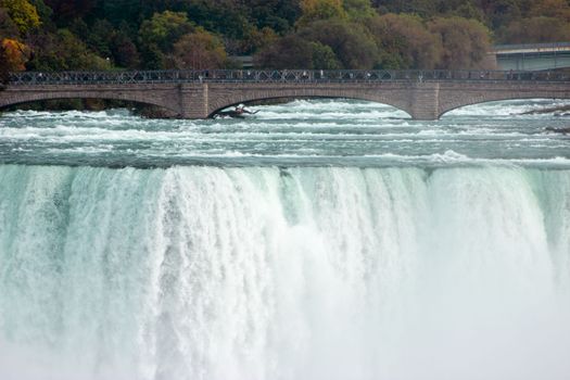 Experience the majestic Niagara Falls cascading with vibrant autumn foliage in the background.