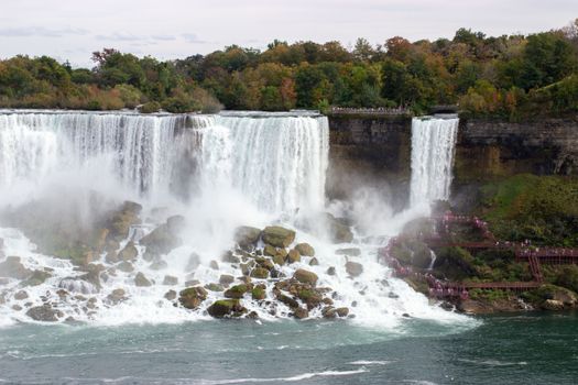 Experience the majestic Niagara Falls surrounded by vibrant autumn foliage and cascading waters.