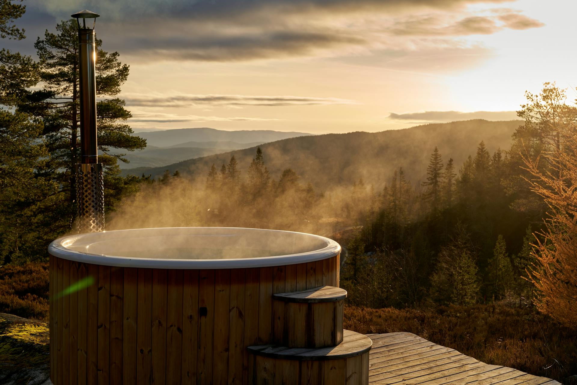 A steaming hot tub amidst the serene Norwegian countryside at sunset, offering stunning views.