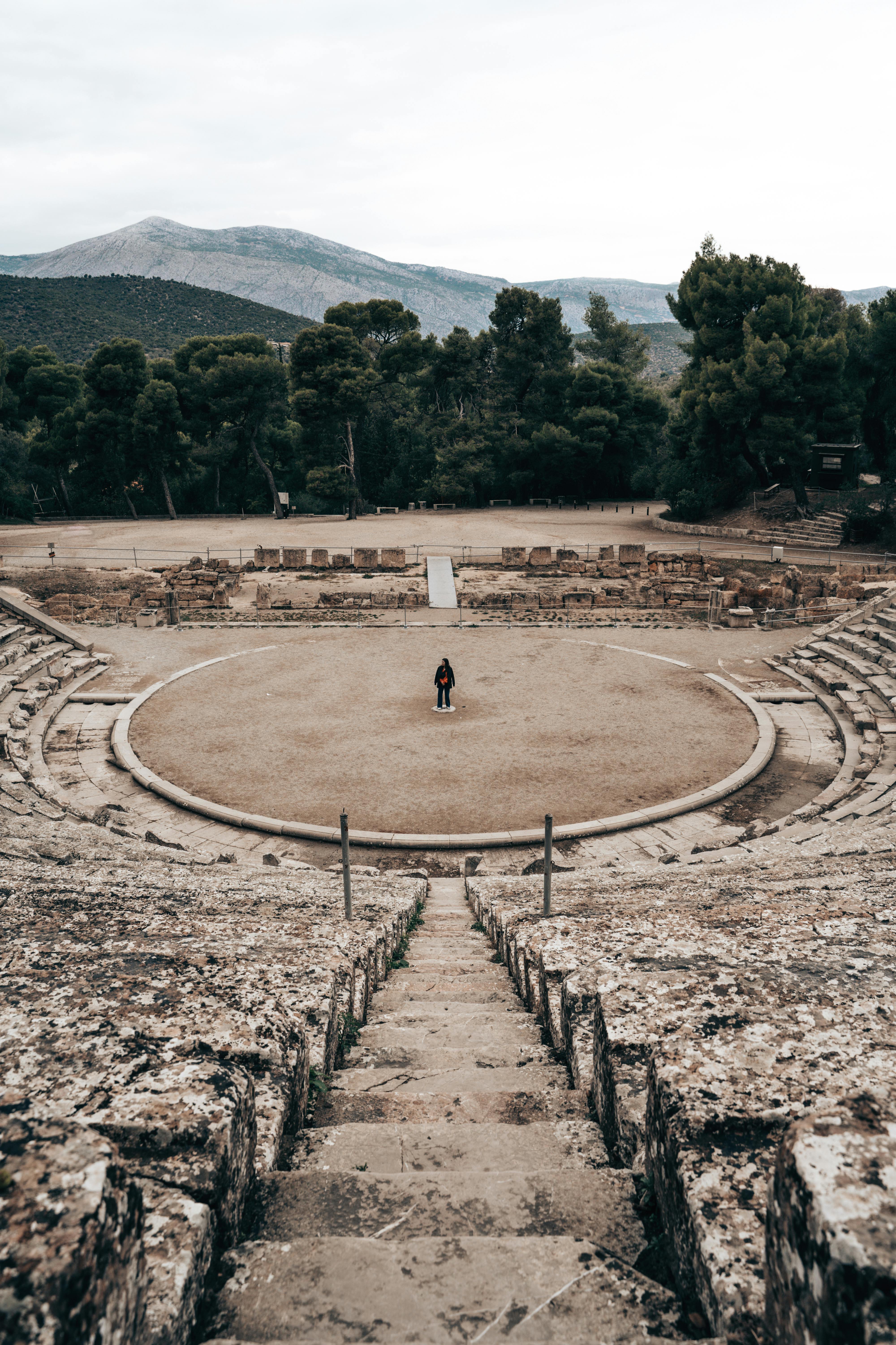 Free A lone person stands in the center of an ancient Greek theater, surrounded by nature. Stock Photo