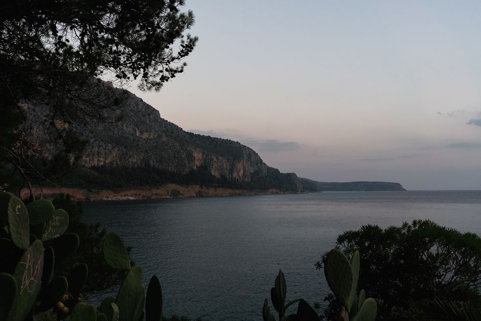 A tranquil view of a coastal cliffside by the sea under a twilight sky.