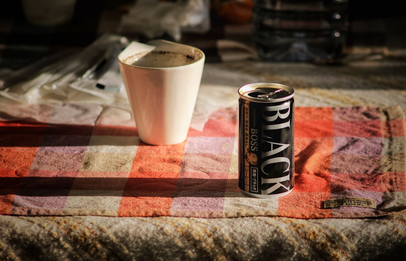 Close-up of a can of black coffee and a porcelain mug on a checkered tablecloth.