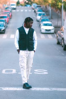 Full-body shot of a fashionable young man with dreadlocks standing on a city street wearing casual streetwear.