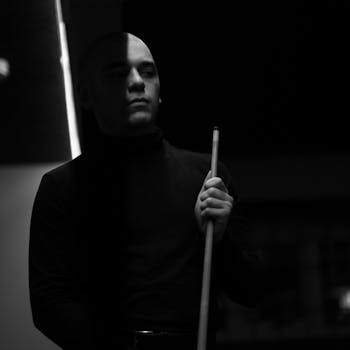 A dramatic black and white portrait of a man holding a pool cue, conveying a serious and focused mood.