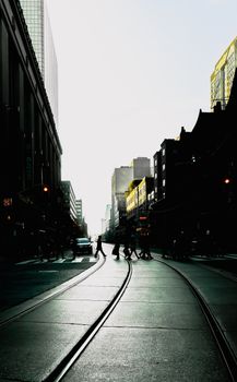 People crossing a city street silhouetted against the rising sun, creating a dramatic urban scene.