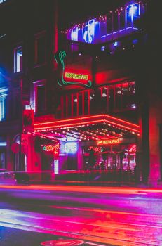 Colorful neon restaurant signs illuminate a bustling city street at night.