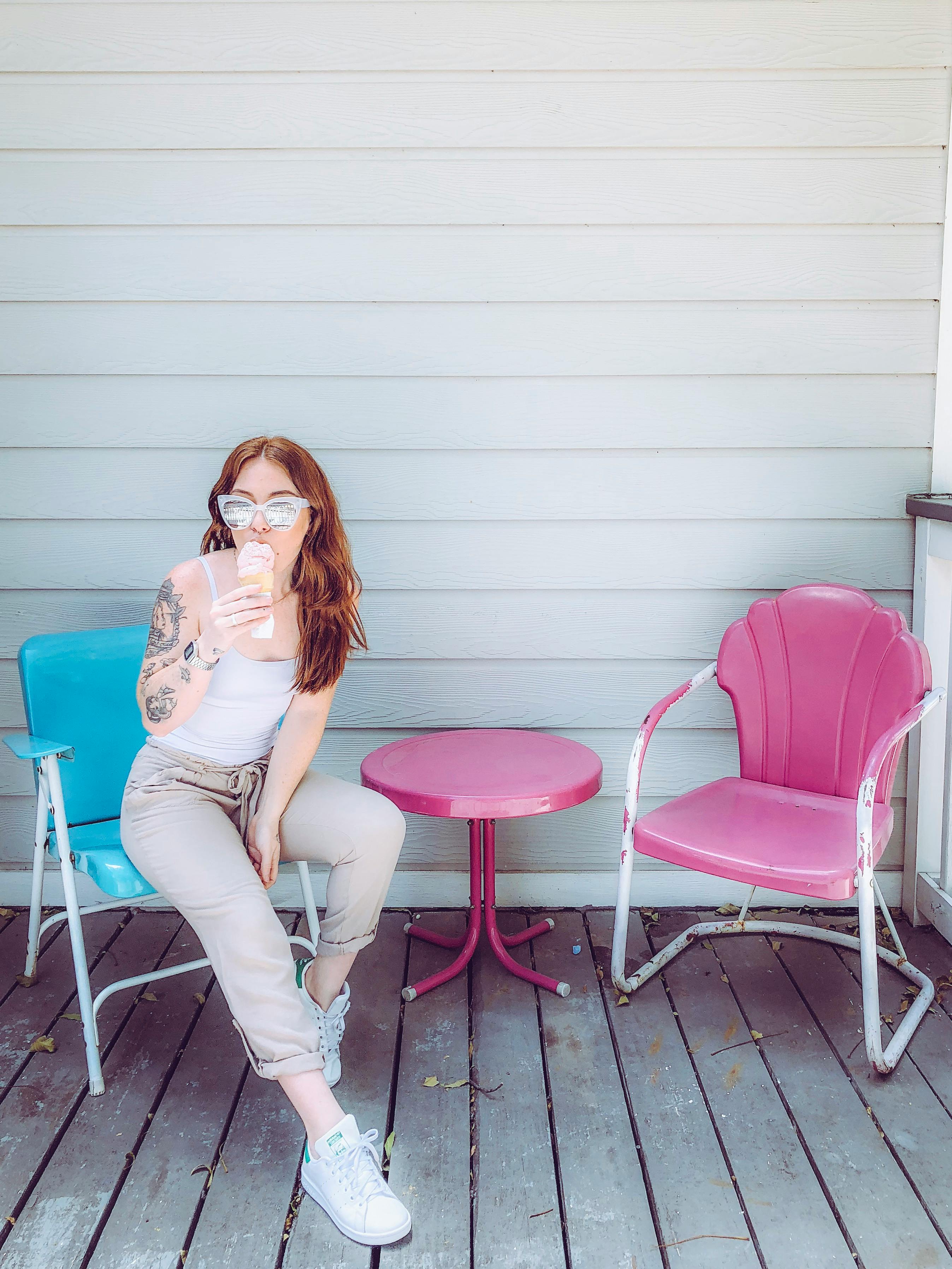 Tattooed woman enjoying ice cream while sitting at a colorful outdoor café on a sunny day.