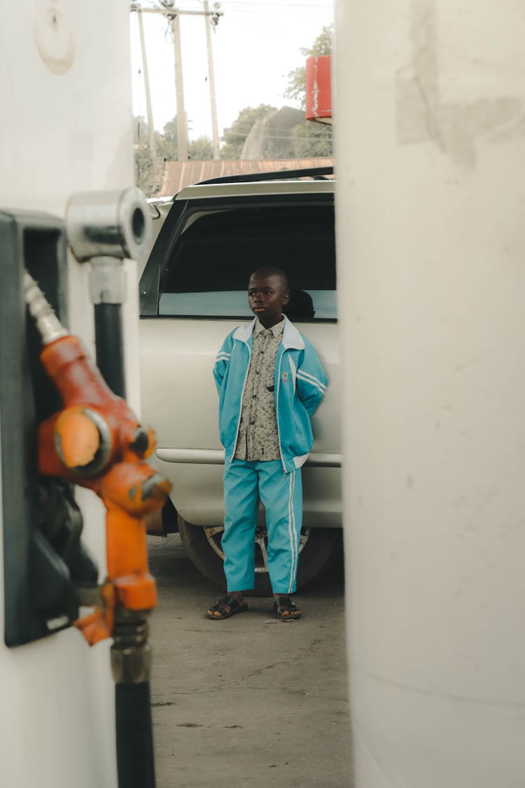 Boy In A Blue Jacket And Blue Jogging Pants Leaning On A Vehicle