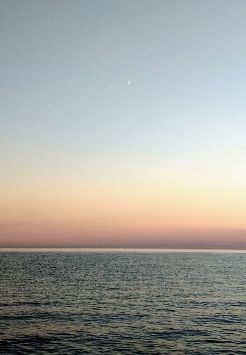 Free Serene ocean view at sunset featuring a crescent moon in the clear sky. Stock Photo