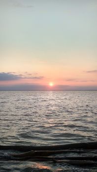 Peaceful sunset over the ocean with gentle waves and pastel sky hues.