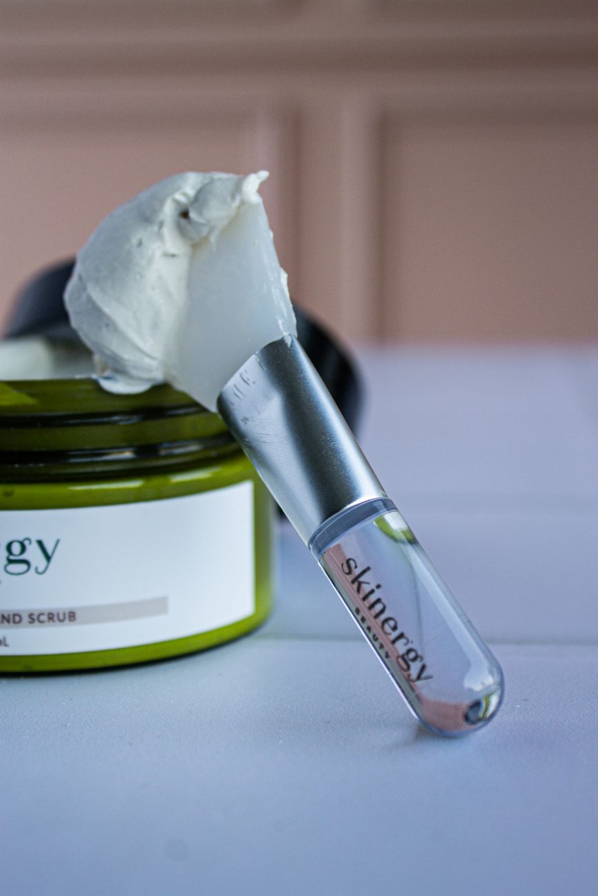 Close-up view of skincare cream in a jar with a brush applicator on a blurred background.