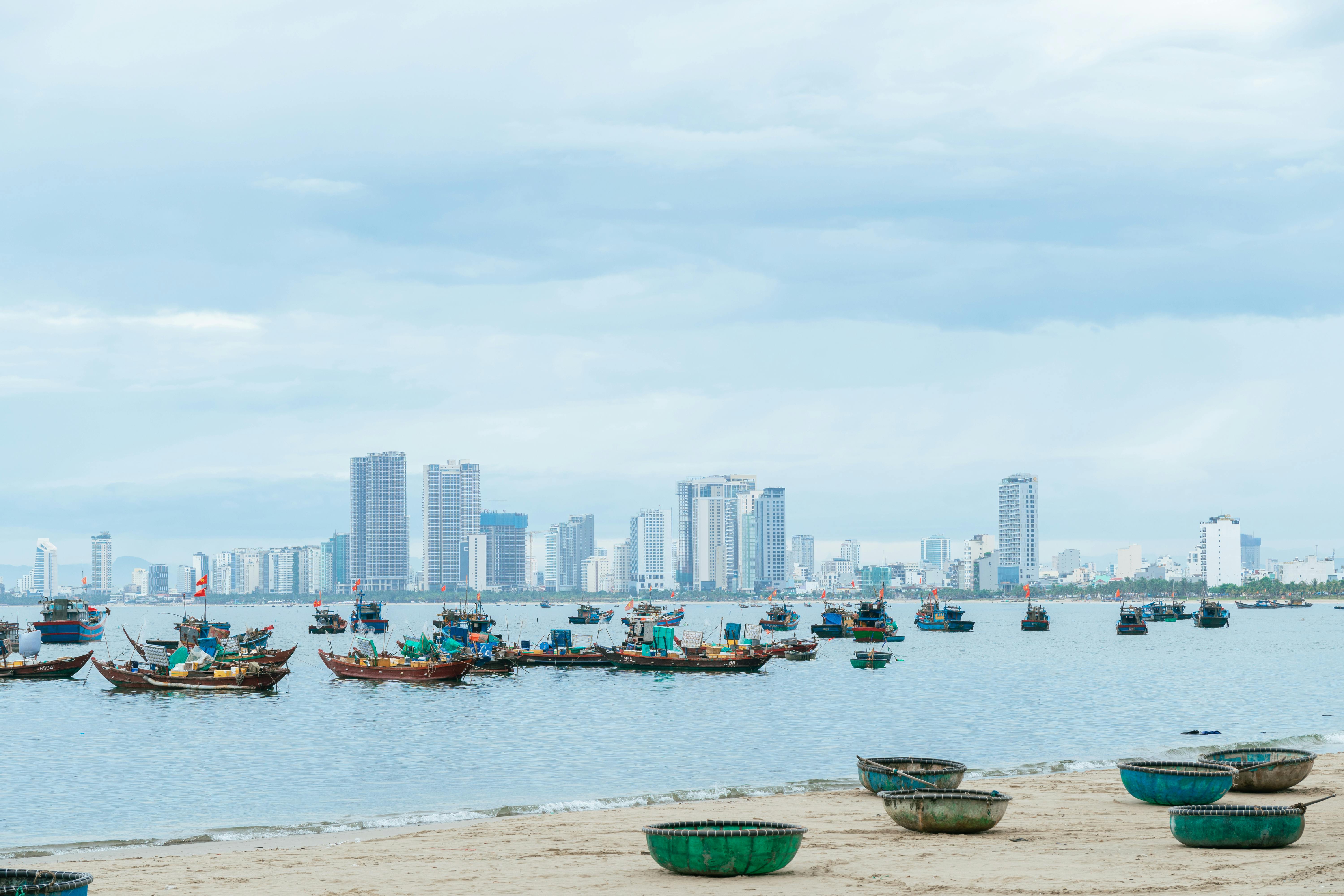 Skyline of a coastal city with traditional fishing boats, under an overcast sky.