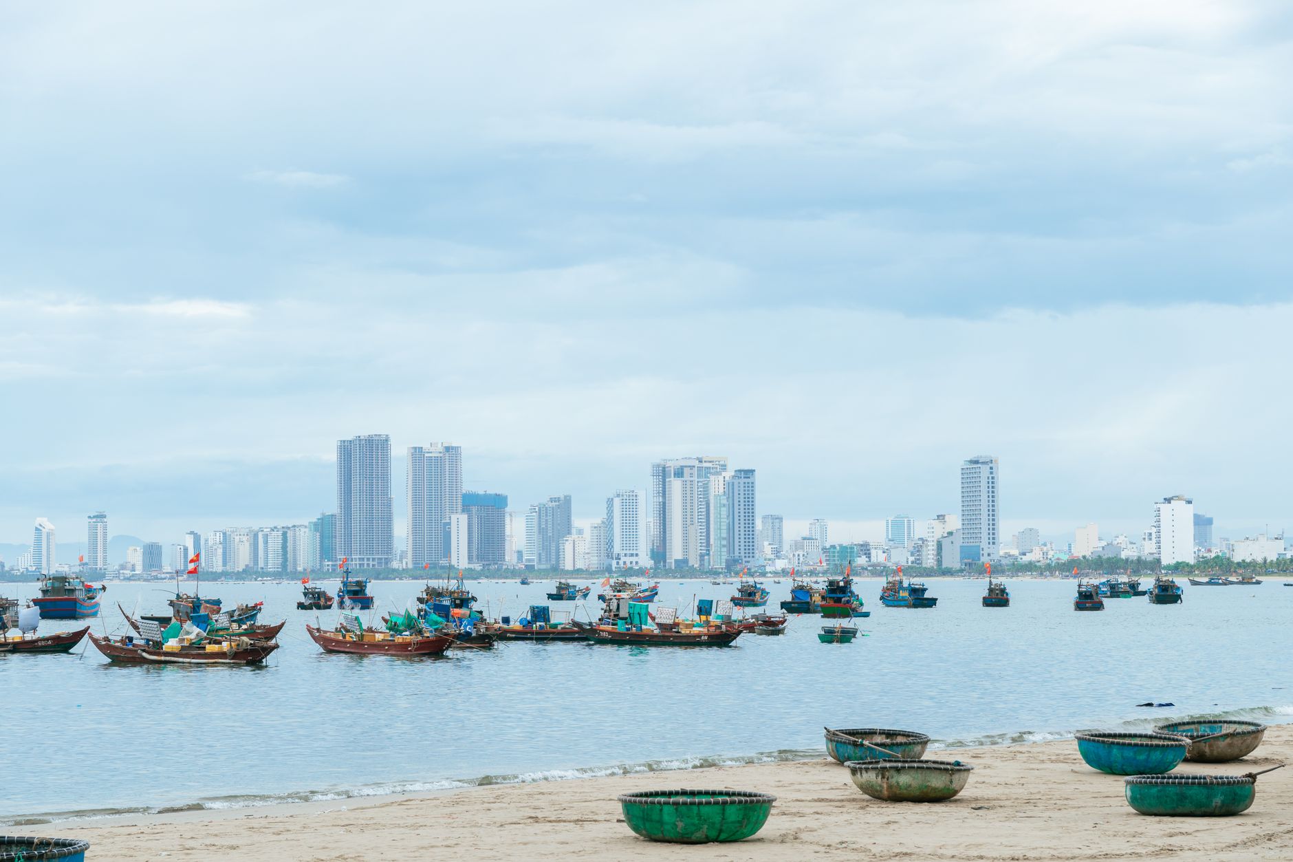 Skyline of a coastal city with traditional fishing boats, under an overcast sky.